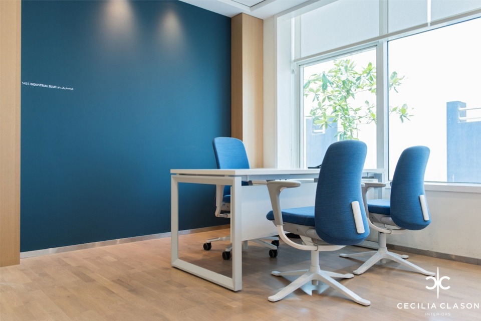 Office Interior Design - Deep blue feature wall with white office desk and white & blue chairs, on wooden flooring